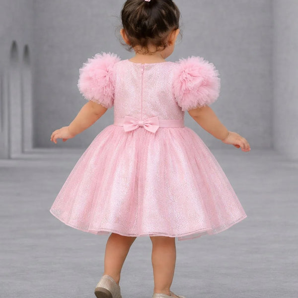 Child wearing a pink dress with fluffy sleeves on a gray background