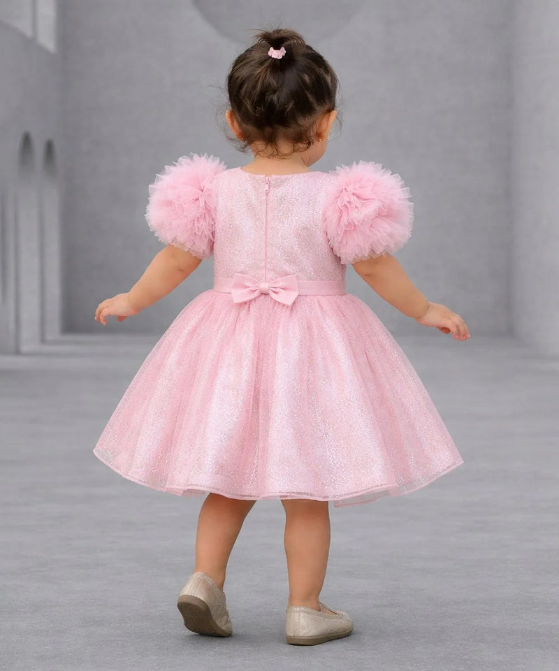 Child wearing a pink dress with fluffy sleeves on a gray background