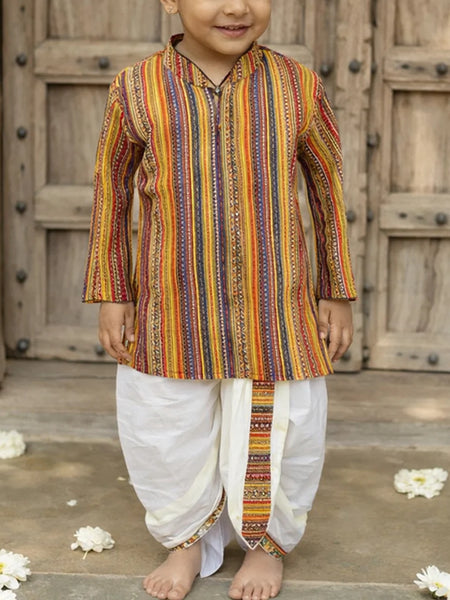 Child wearing a colorful striped kurta with white dhoti standing in front of wooden doors.
