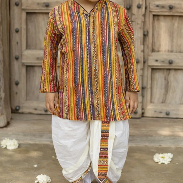 Child wearing a colorful striped kurta with white dhoti standing in front of wooden doors.