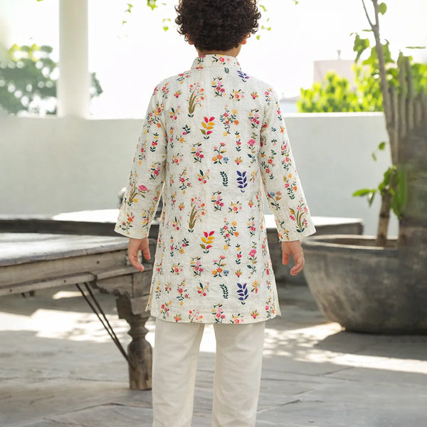 Child wearing a floral embroidered kurta with white pants outdoors.