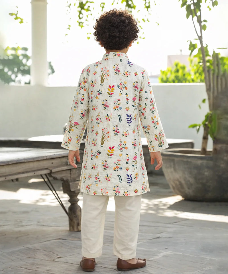 Child wearing a floral embroidered kurta with white pants outdoors.