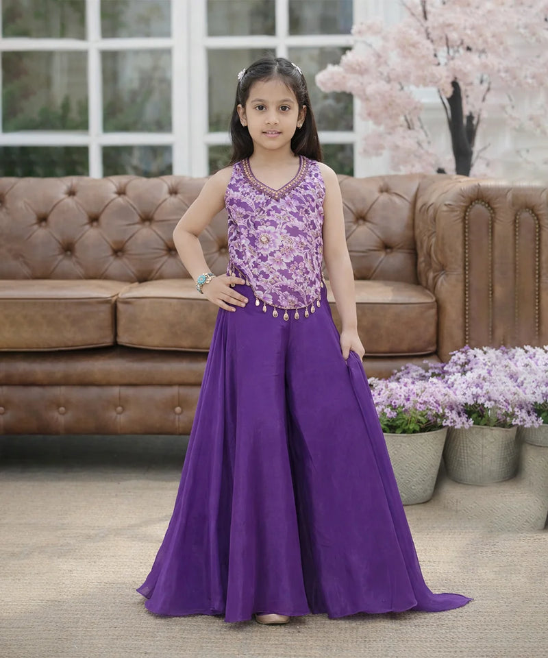 Young girl in a purple dress standing in front of a brown sofa with decorative elements.