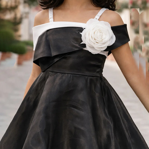 Black dress with white floral detail worn by a person, blurred background
