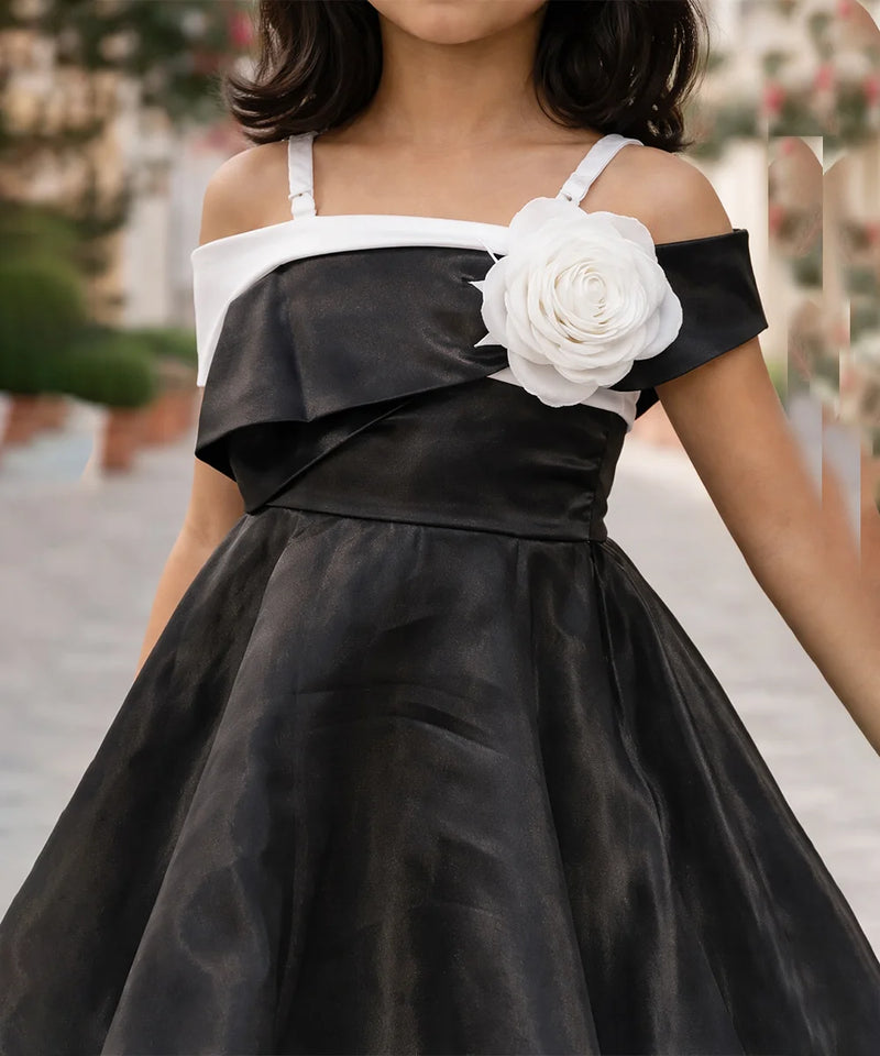 Black dress with white floral detail worn by a person, blurred background