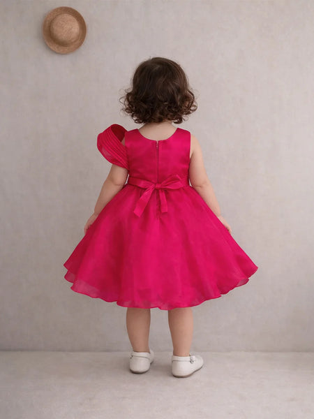 Child wearing a bright pink dress with a bow, standing against a plain background.