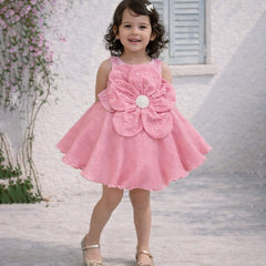 Young girl in a pink dress with a large flower design standing outdoors.