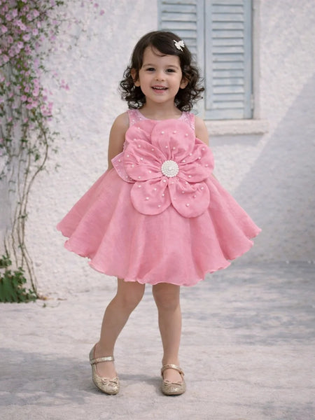 Young girl in a pink dress with a large flower design standing outdoors.