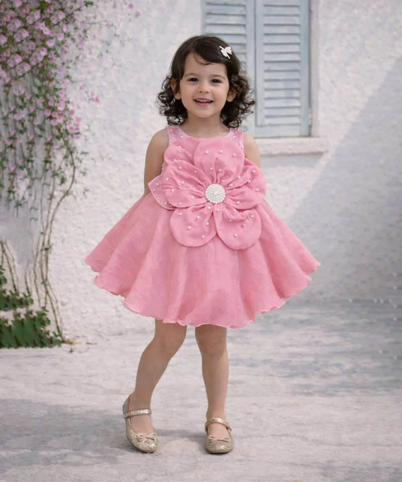Young girl in a pink dress with a large flower design standing outdoors.
