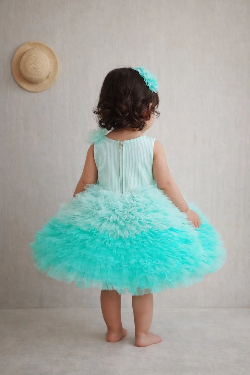 Child wearing a turquoise dress with a ruffled skirt, standing against a plain background.