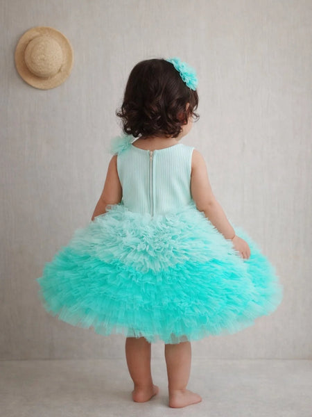Child wearing a turquoise dress with a ruffled skirt, standing against a plain background.