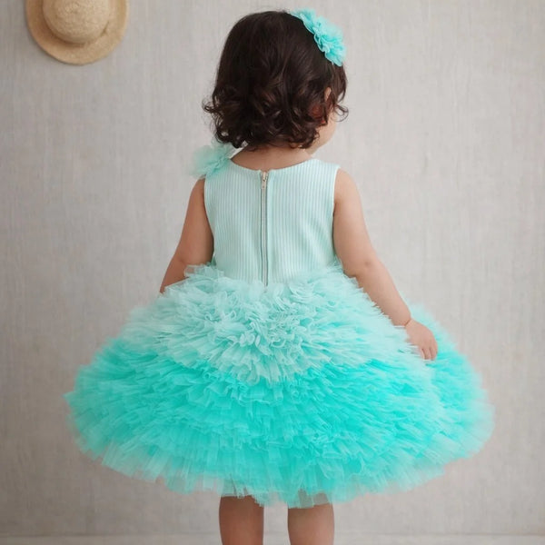 Child wearing a turquoise dress with a ruffled skirt, standing against a plain background.