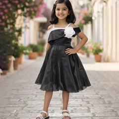 Young girl in a black and white dress with a flower detail standing on a paved walkway.
