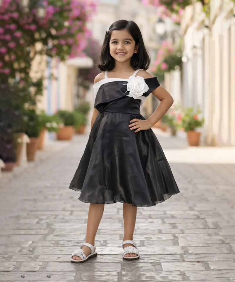 Young girl in a black and white dress with a flower detail standing on a paved walkway.