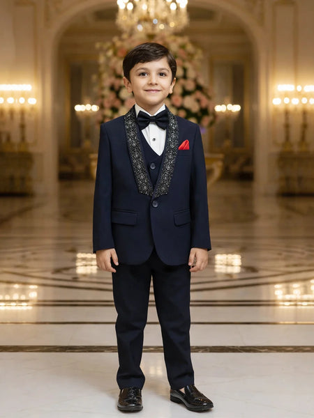 Young boy in a formal navy suit standing in an elegant room with chandeliers.