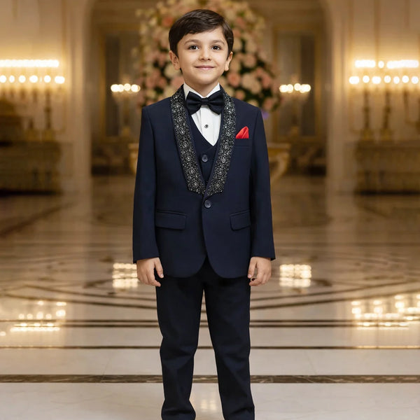 Young boy in a formal navy suit standing in an elegant room with chandeliers.