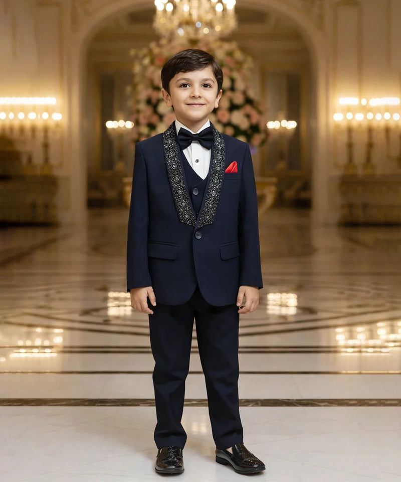 Young boy in a formal navy suit standing in an elegant room with chandeliers.