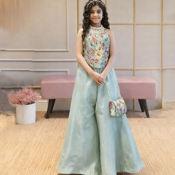 Woman in a floral top and light blue skirt holding a matching handbag in an indoor setting.