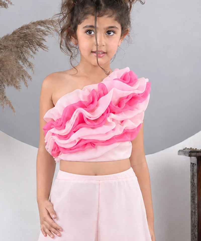 Young girl wearing a pink ruffled top and light pink skirt against a gray background