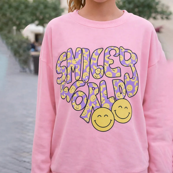 Person wearing a pink sweatshirt with 'Smiley World' design outdoors.