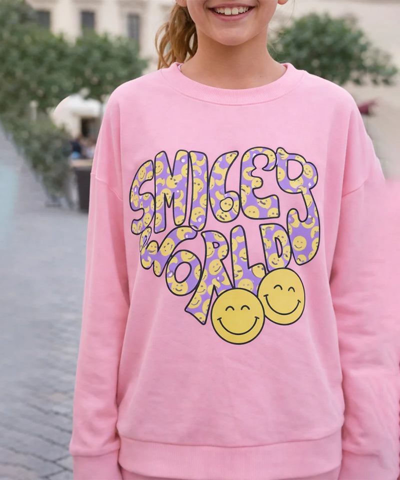 Person wearing a pink sweatshirt with 'Smiley World' design outdoors.