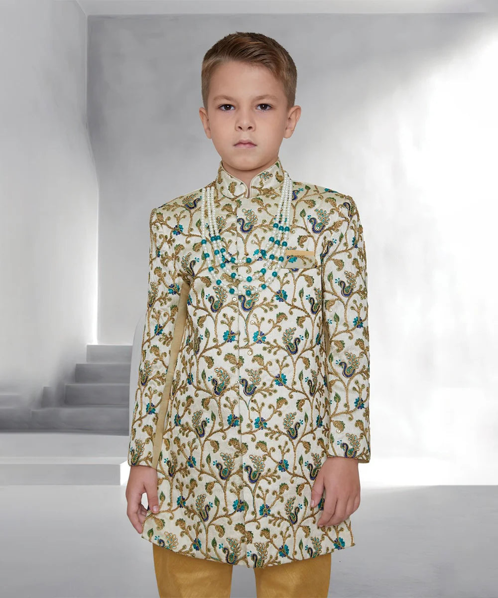 This designer sherwani for boys consists of a self-embroidered Sherwani and a mustard Colored Pyjama. It features a pocket square and stylized buttons on the sherwani that uplift the entire look.