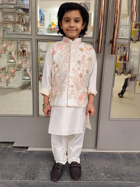 Child wearing a cream color kurta pajama with a jacket  traditional outfit standing in front of a store entrance.
