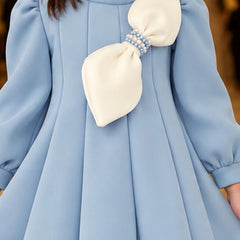 A close-up of a light blue dress with a large cream bow on the chest, featuring a pearl-like beaded band at the center of the bow.