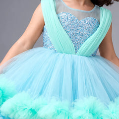 A child wearing a sleeveless light blue and mint green sequined ball gown with a sheer mesh bodice and a voluminous tulle skirt.