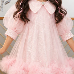 A young girl wearing a light pink sequined tulle dress with a large embellished Peter Pan collar, puff sleeves, and a ruffled tulle hem.