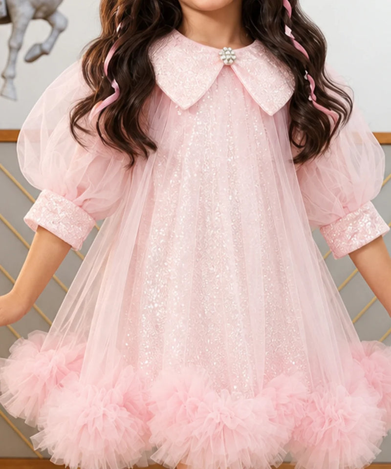 A young girl wearing a light pink sequined tulle dress with a large embellished Peter Pan collar, puff sleeves, and a ruffled tulle hem.