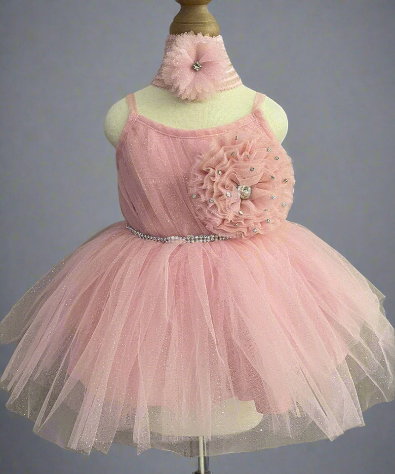 It's a peach Colored frock that features shinny lace, big flower and pleated detailing. Moreover, it comes with an attached belt to be tied at the back.