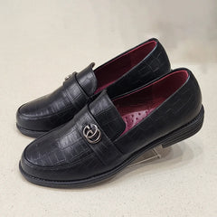Black leather loafers with a decorative buckle on a light gray background