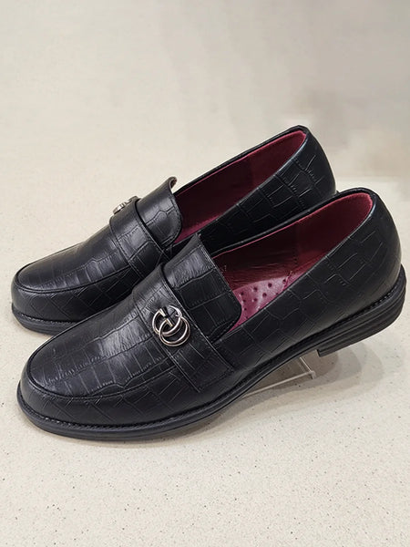 Black leather loafers with a decorative buckle on a light gray background