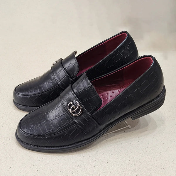 Black leather loafers with a decorative buckle on a light gray background