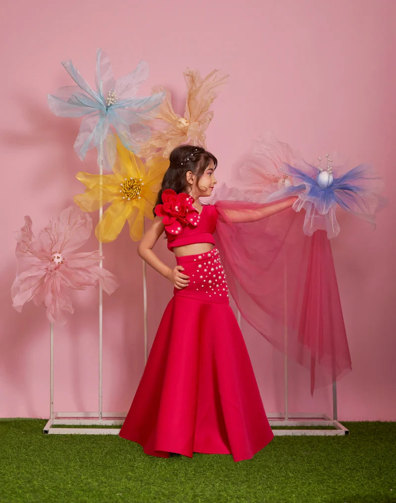 This Pink Coloured birthday party wear dress for kids consists of a crop top, a asymmetric skirt and a dupatta. It features a big flower on the crop top and pearl detailing on it and on the skirt that elevates the entire look.
