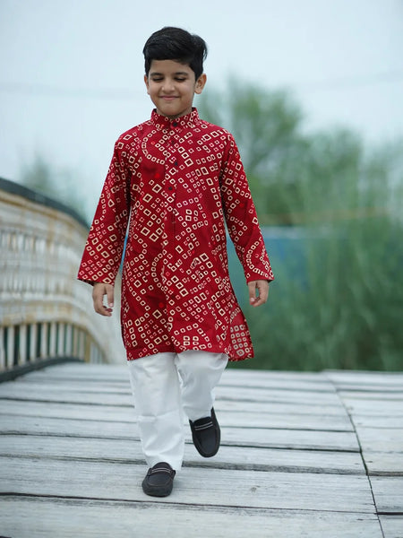 Child wearing a red patterned kurta with white pants walking on a wooden deck.