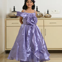 Young girl wearing a purple dress with a large flower detail in a room.
