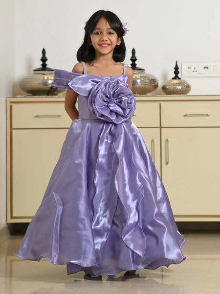 Young girl wearing a purple dress with a large flower detail in a room.