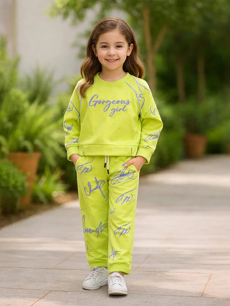Young girl in a bright green outfit with 'Gorgeous girl' text, standing outdoors on a wooden path.