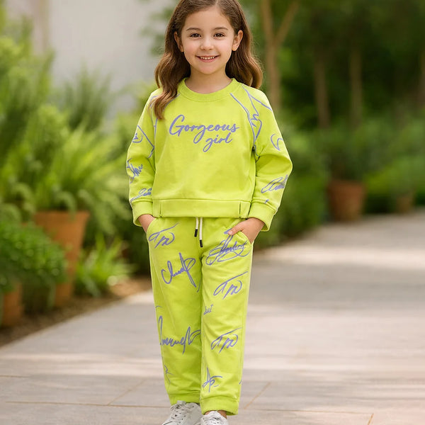 Young girl in a bright green outfit with 'Gorgeous girl' text, standing outdoors on a wooden path.