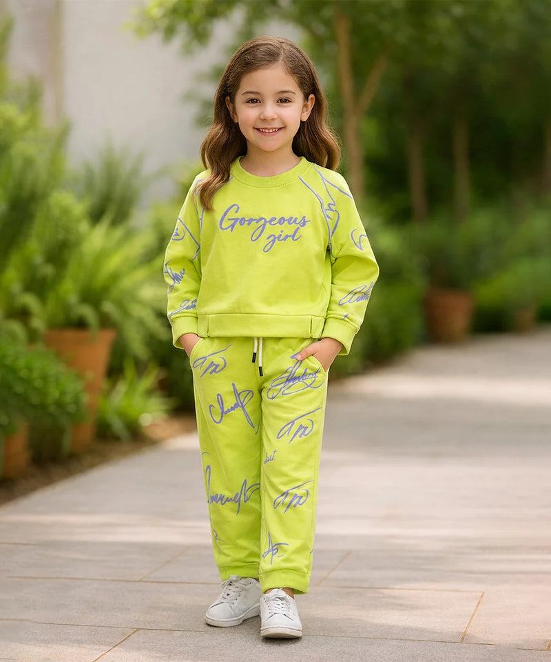 Young girl in a bright green outfit with 'Gorgeous girl' text, standing outdoors on a wooden path.