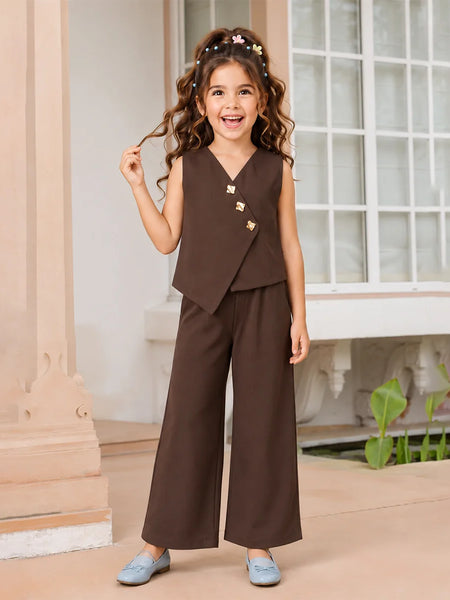 A young girl with curly brown hair wearing a dark brown two-piece outfit consisting of a sleeveless wrap vest with gold buttons and matching wide-leg trousers, paired with light blue shoes, standing in a classic indoor setting with a window and columns.