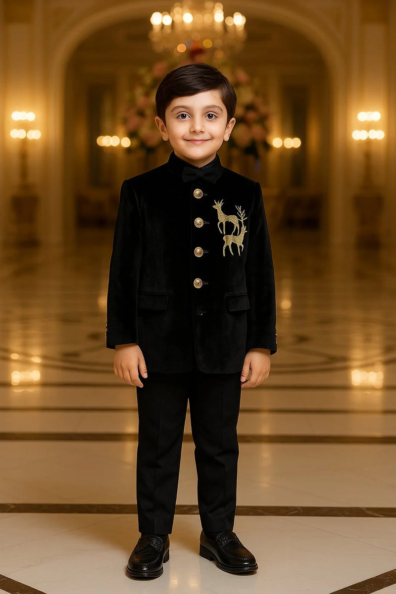 Young boy in a formal black suit with a deer emblem standing in an elegant hall.