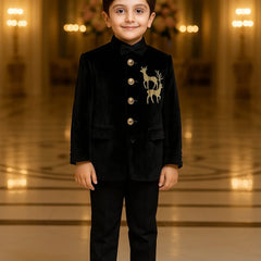 Young boy in a formal black suit with a deer emblem standing in an elegant hall.