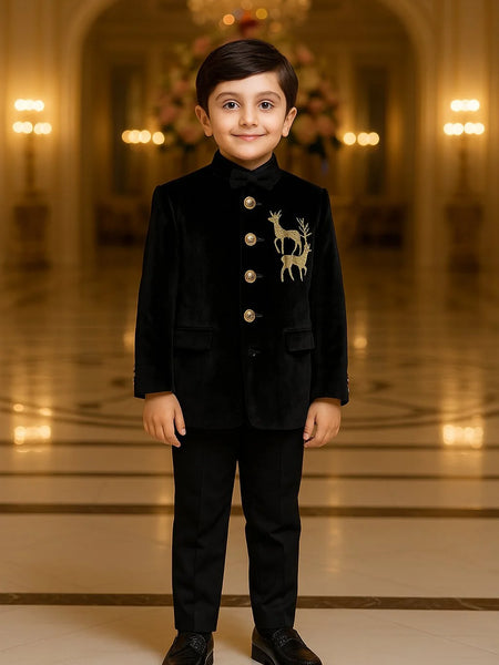 Young boy in a formal black suit with a deer emblem standing in an elegant hall.