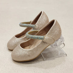 Pair of glittery gold shoes with rhinestone straps on a light beige background