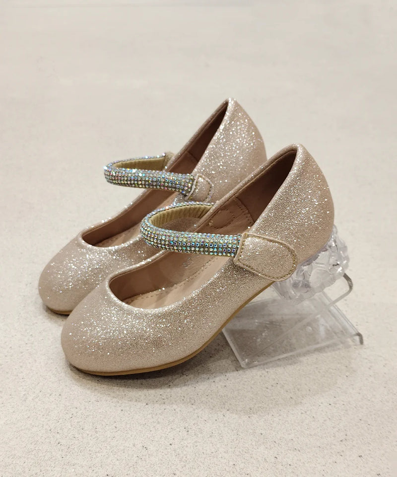 Pair of glittery gold shoes with rhinestone straps on a light beige background