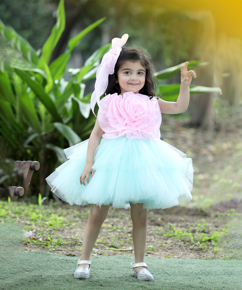 A young girl wearing a pink and white floral dress with a tutu skirt, standing in a garden setting.