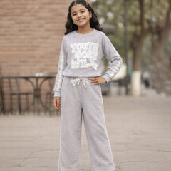 Young girl wearing a gray sweatshirt and pants with text, standing outdoors.